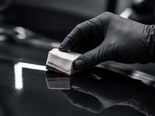 An applicator spreading ceramic coating across a black bonnet