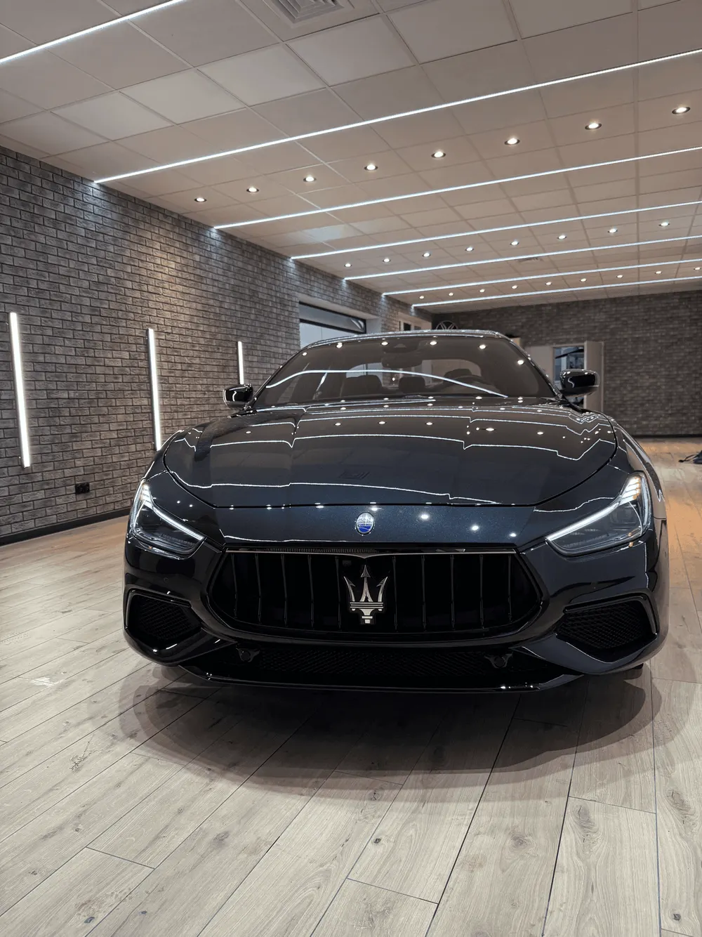 Die Front eines schwarzen Maserati im Studio — Leuchten spiegeln sich gleichmäßig im Lack