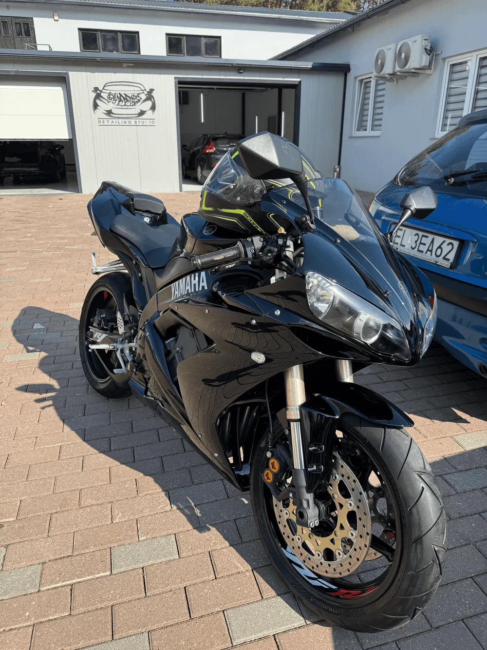 Eine Yamaha R6 auf dem Pflaster vor dem Buddies Studio, neben einem Auto
